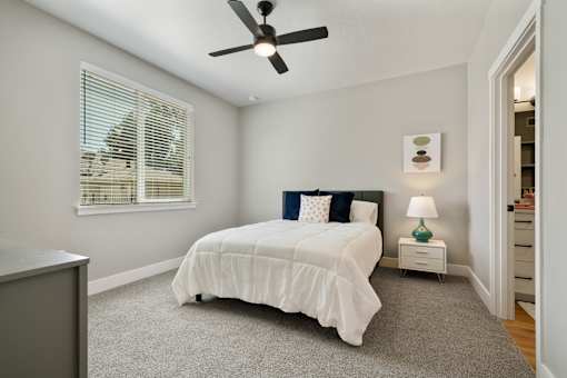 A bedroom with a white bed and a ceiling fan.