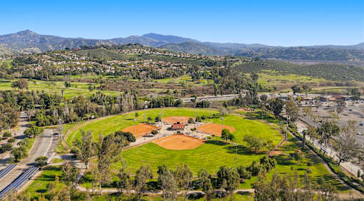A baseball field is surrounded by trees and a road.
