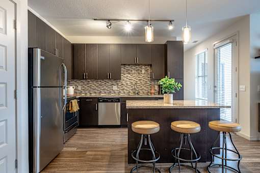 A kitchen with a refrigerator, a counter, and bar stools.