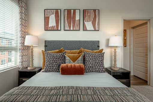 A bedroom with a bed, two lamps, and three framed artworks on the wall.