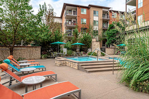 A pool area with sun loungers and umbrellas in front of a building.