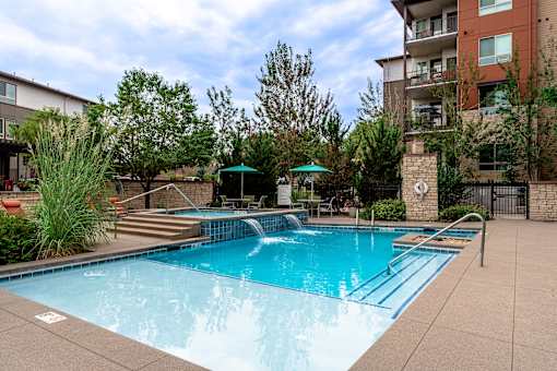 A swimming pool surrounded by a concrete patio and a building in the background.