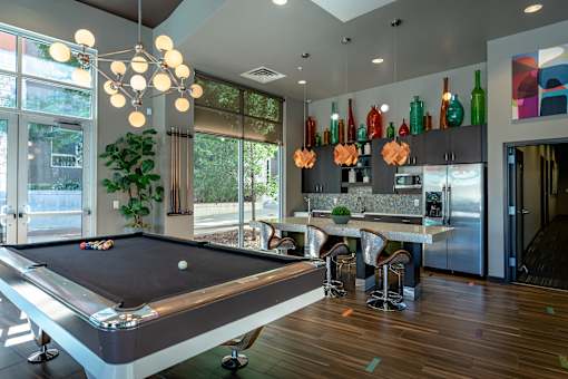 A pool table is in the middle of a room with a bar and a dining table.