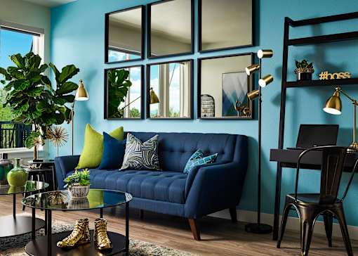 A living room with a blue couch, a glass table, and a mirror on the wall.