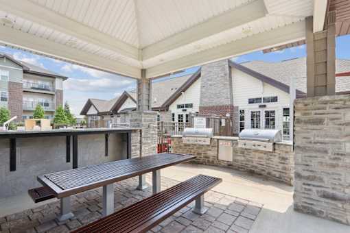 A patio with a table and benches under a roof.