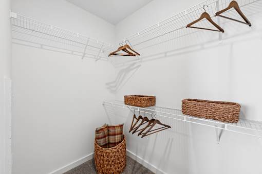 A white closet with clothes hanging and baskets on the shelves.