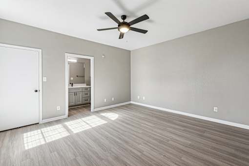 A room with a ceiling fan and light, hardwood floors, and a white door.