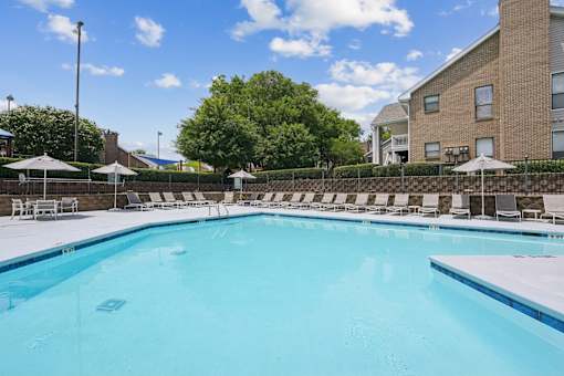 A large swimming pool with a blue tinted water and white lounge chairs around it.