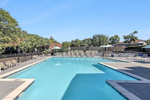 A large outdoor swimming pool surrounded by lounge chairs and trees.