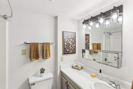 A white bathroom with a toilet, sink, mirror, and lights.