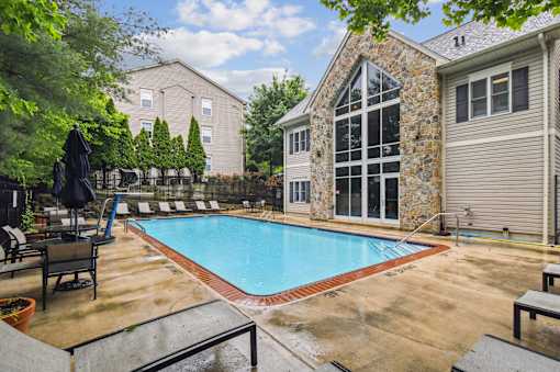 A pool surrounded by a patio and a stone building.