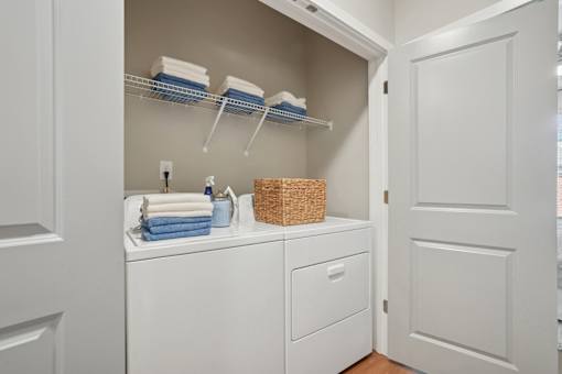 A white laundry room with a washer and dryer, a basket, and towels.