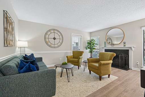 A living room with a grey couch, a yellow chair, a black chair, a small table, a fireplace, and a mirror on the wall.