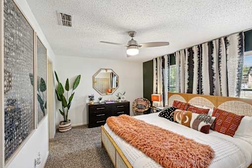 A bedroom with a bed, dresser, mirror, and a plant.