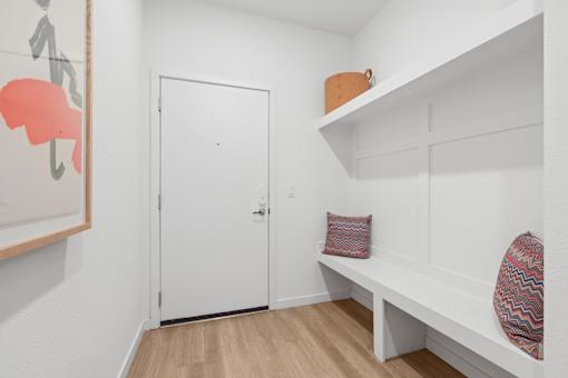 A white door is in a room with a bench and a shelf.