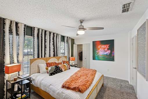A bedroom with a bed, a ceiling fan, and a painting on the wall.