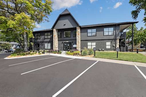 A parking lot in front of a grey building with a black fence.
