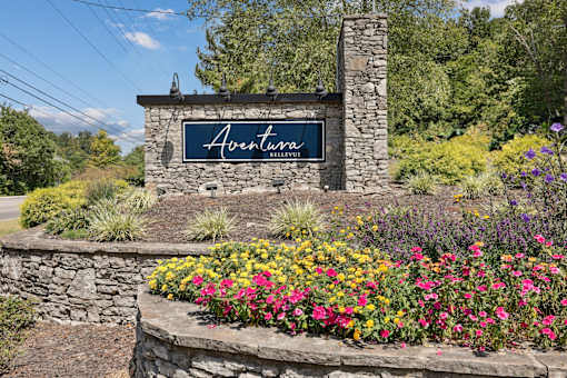 A stone wall with a sign that says Aventura in front of a field of flowers.