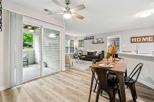 A dining room with a table set for two and a sliding glass door leading to a backyard.