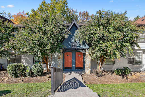 A house with a red door is surrounded by trees and bushes.