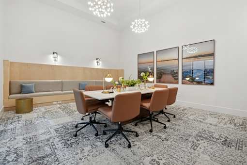 An interior view of a kitchen with a kitchen island countertop with a kitchen sink, kitchen cabinetry, overhead light fixtures, and a stainless steel dishwasher, with views of a living room with a couch, wall artwork, a ceiling fan, front-end table, and a dual patio entryway doors at The One at Columbia apartments for rent in Columbia, SC