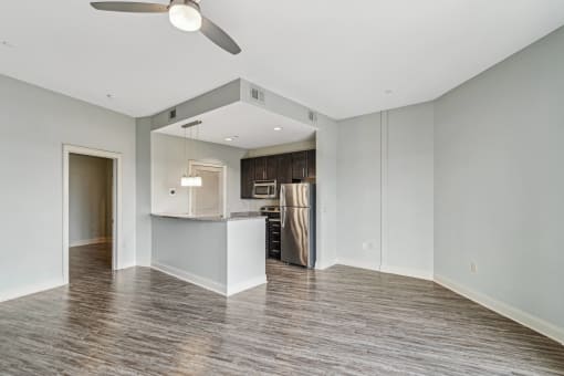 an empty living room with a kitchen and a ceiling fan