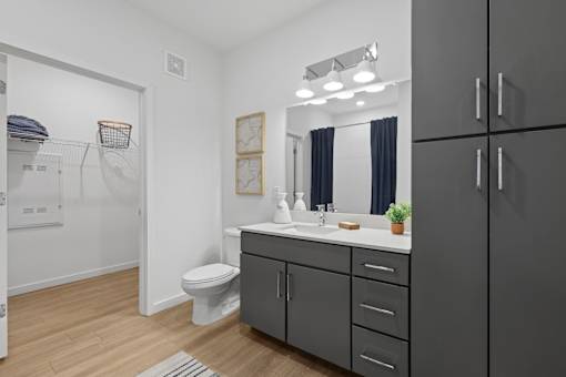 A bathroom with a white toilet, sink, and grey cabinets.