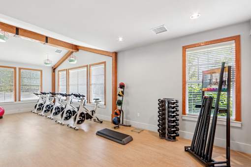 A room with a row of exercise bikes and a rack of dumbbells.
