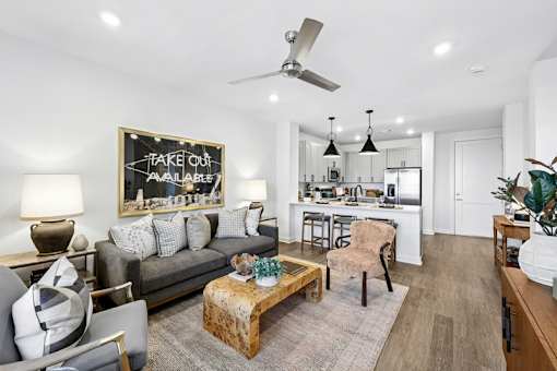 A living room with a grey couch, a wooden coffee table, and a chalkboard sign that says "TAKE OUT AVAILABLE".