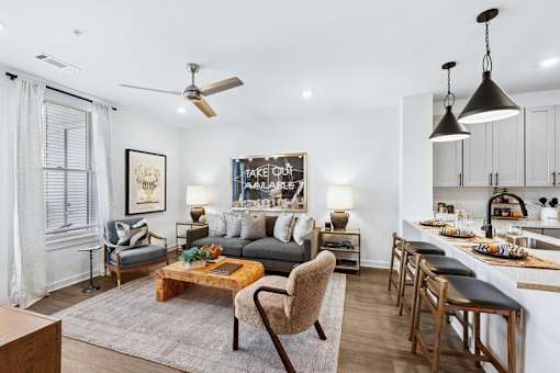 A modern living room with a grey sofa, a wooden coffee table, and a kitchen area in the background.