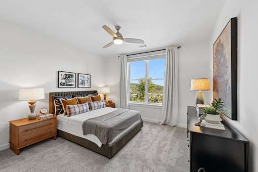 A bedroom with a large bed, a ceiling fan, and a view of the outdoors through a window.