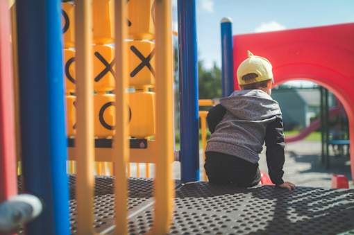 A child in a grey hoodie and yellow hat is sitting on a playground slide.
