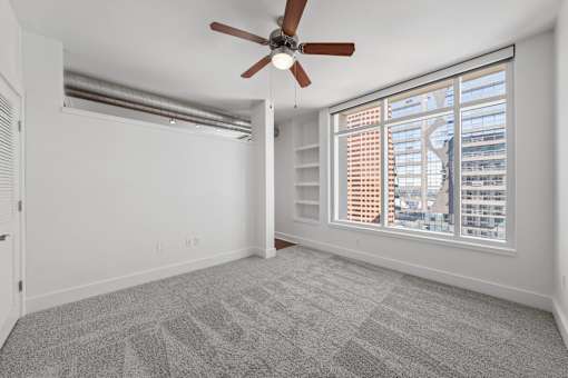 A room with a ceiling fan and a large window with blinds.