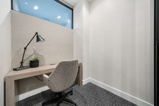 A grey chair is in front of a desk with a lamp and a plant on it.