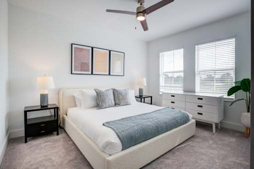 A bedroom with a large bed, a ceiling fan, and a nightstand with a lamp.