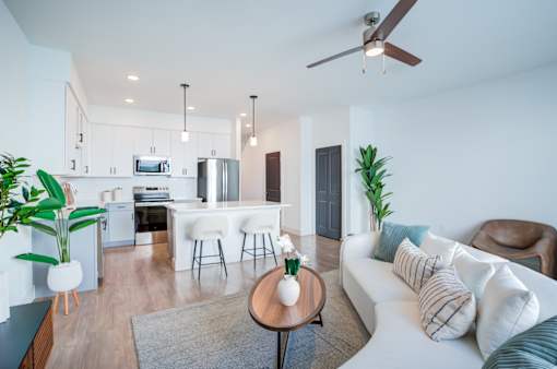 A modern living room with a white sofa and a kitchen in the background.