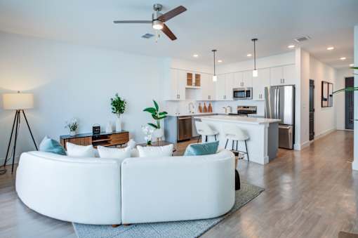 A modern living room with a white sofa and a kitchen in the background.