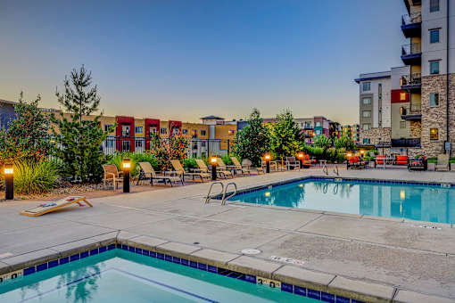 A swimming pool surrounded by chairs and trees with apartment buildings in the background.