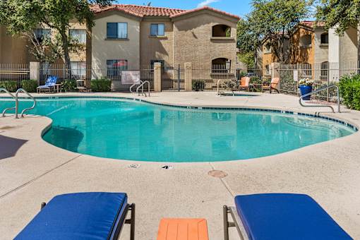 A swimming pool with blue loungers and orange sunshades.