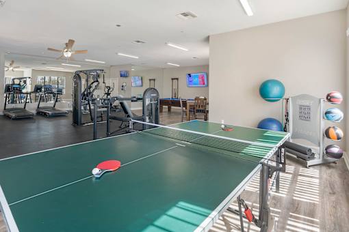 A ping pong table is in the middle of a room with exercise equipment.