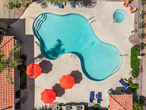 An aerial view of a pool with a blue water feature and orange umbrellas.