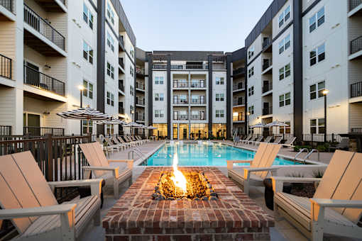 A pool surrounded by lounge chairs and umbrellas in a courtyard.