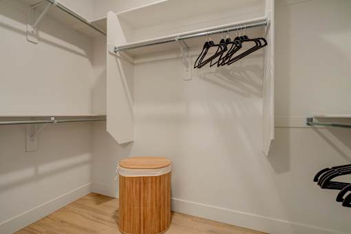 A white closet with a wooden trash can under a hanging rod.