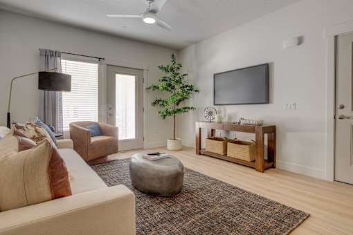 A living room with a couch, a chair, a coffee table, a television, and a plant.
