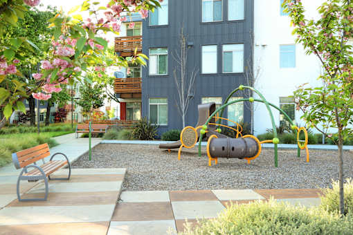 A playground with a slide, swings, and a bench in front of a building.