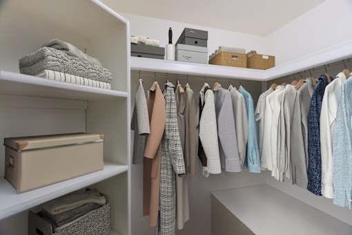 A white closet with clothes hanging and folded items on shelves.