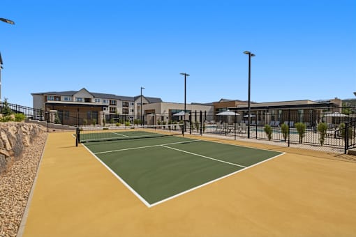 A tennis court is surrounded by a fence and a building.