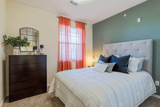 A bedroom with a large bed, a wooden dresser, and a window with orange curtains.