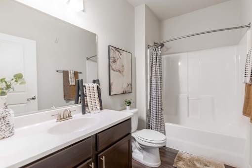 A white sink and toilet in a bathroom with a white tub and a grey shower curtain.