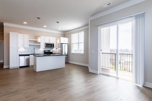 an empty living room with a balcony and a kitchen in the background